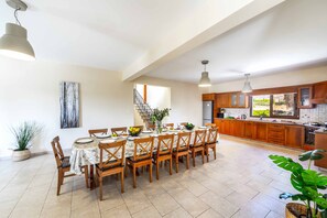 Un comedor amplio con una mesa larga y sillas, una cocina con armarios de madera, y una escalera que lleva a otro nivel.