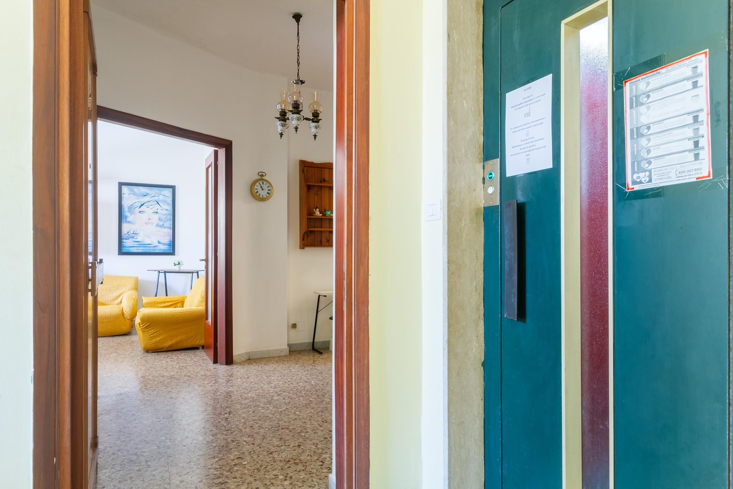 A hallway with a wooden door, a clock, and a framed picture on the wall.
