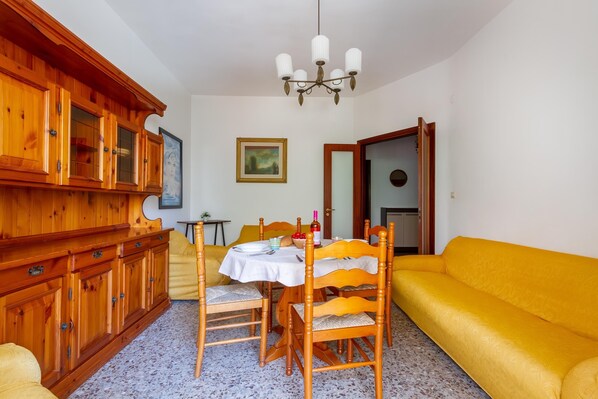 Un coin repas avec des meubles de rangement en bois, une table dressée pour quatre personnes et un canapé jaune.