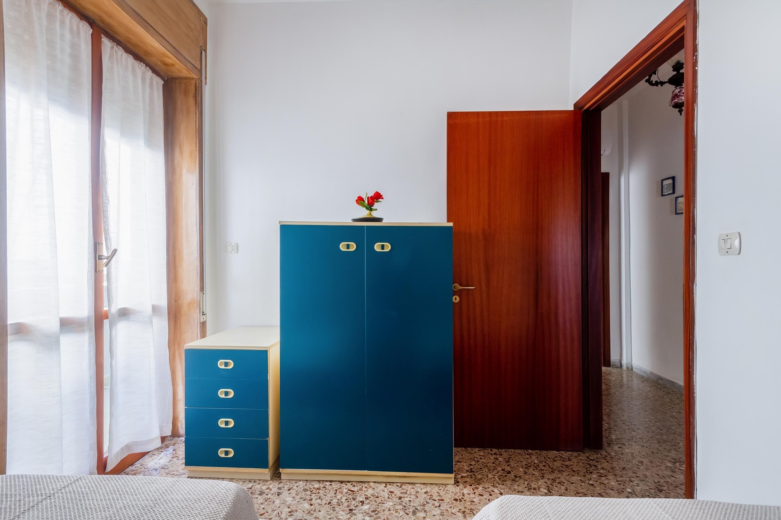 A room with a blue wardrobe, a wooden door, and a window with curtains.