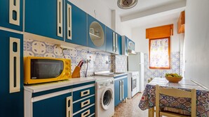 Een praktische keuken met een wasmachine, magnetron en een eethoek met een tafel en stoelen.