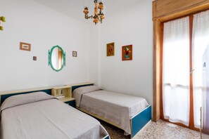 Une chambre avec deux lits simples, une armoire en bois, un miroir et un lustre.