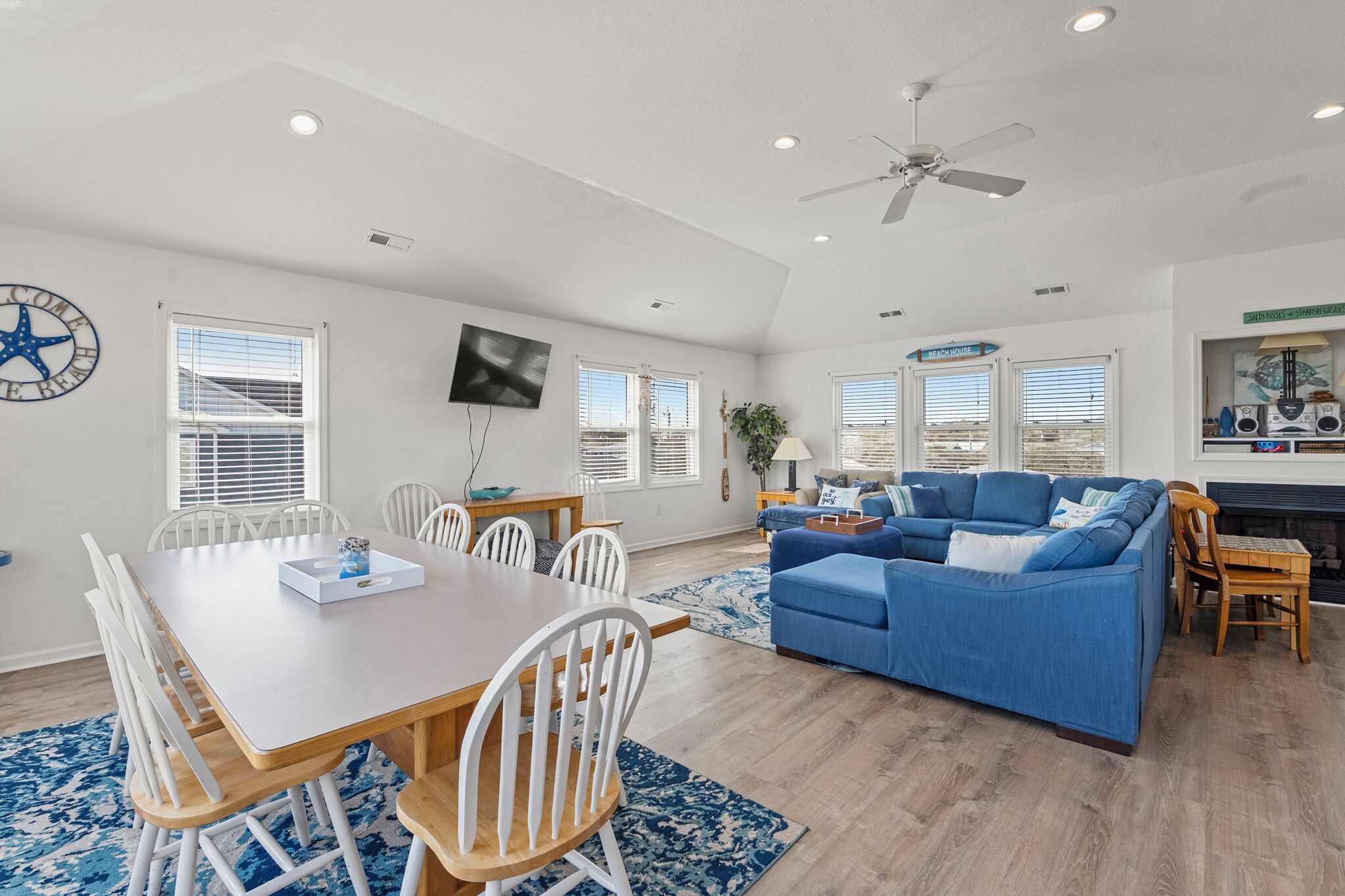A spacious living room with a dining area, a blue sofa, a ceiling fan, and a fireplace.