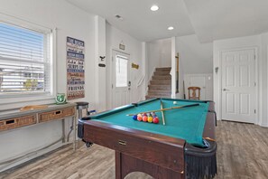Una mesa de billar con bolas, una ventana con persianas, una escalera y una puerta.