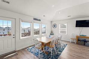 Un comedor con una mesa grande, sillas blancas, un tapete azul y un letrero que dice 'BEACH HOUSE'.