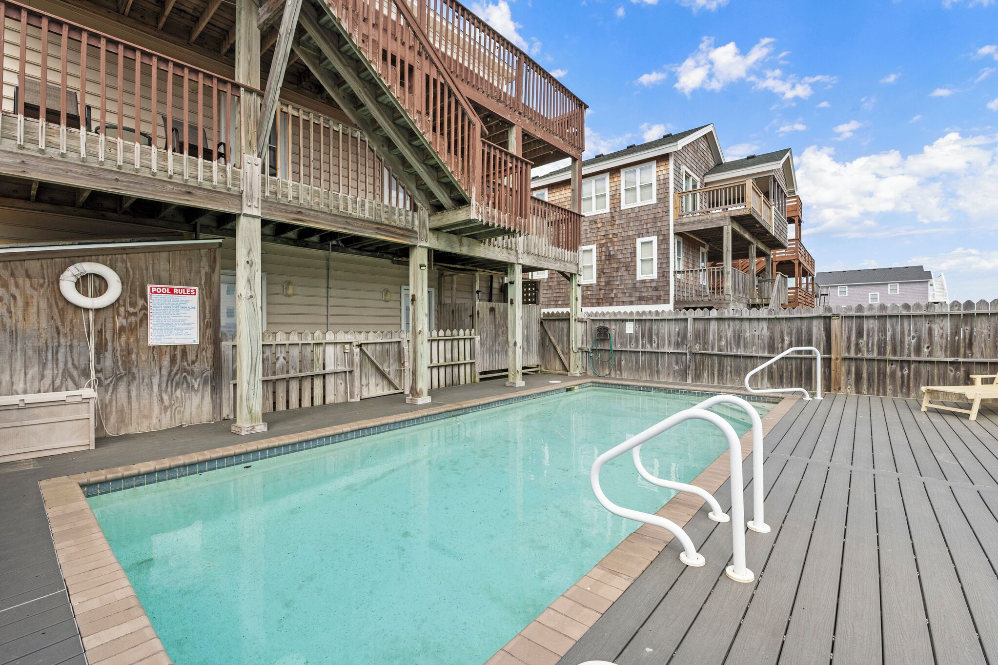 Une terrasse en bois avec une piscine, des rampes en bois et un panneau indiquant les règles d’utilisation de la piscine.