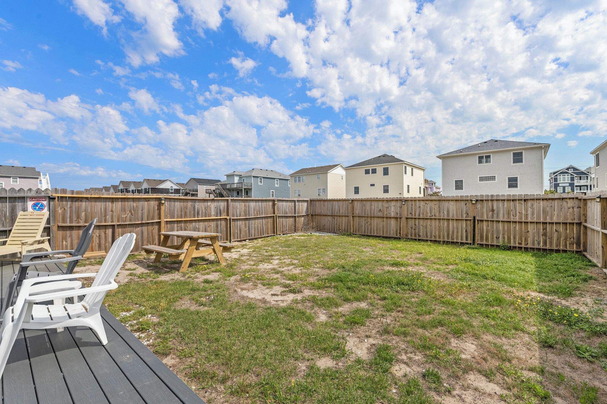 A backyard with a wooden deck, a picnic table, and several Adirondack chairs.