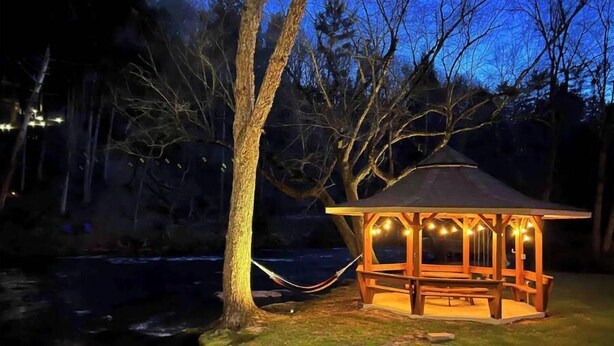 Gazebo con tetto e pareti, immerso tra alberi e prato.