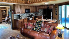 Un'ampia zona giorno in stile loft con soffitto alto, travi in legno, un divano in pelle con cuscini floreali, un tavolo da pranzo per quattro e una cucina con mobili in legno e un piano di lavoro in marmo.