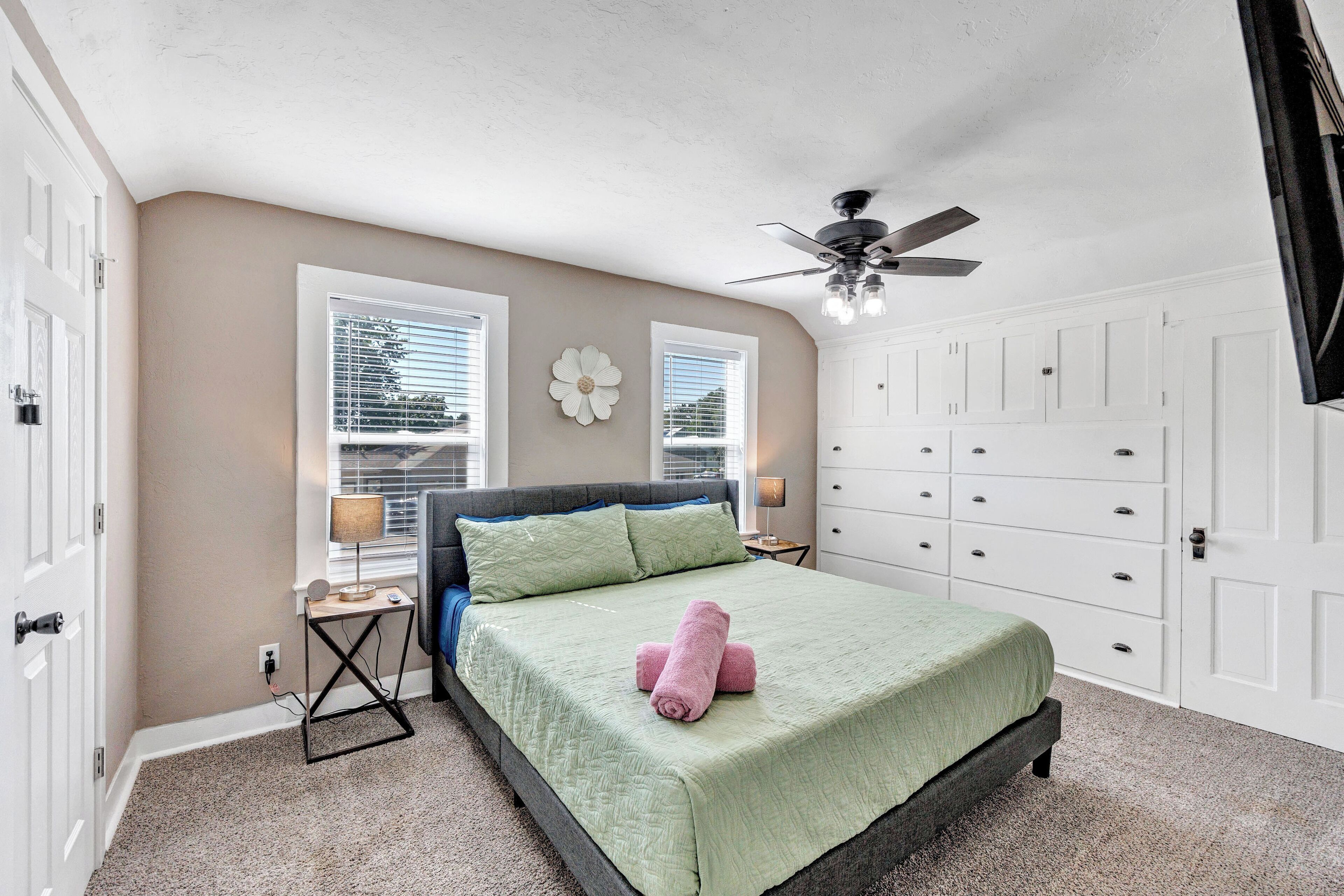 A bedroom with a bed, a ceiling fan, and a dresser.