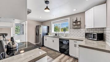 A modern kitchen with white cabinets, a stainless steel refrigerator, a microwave, and a dishwasher.