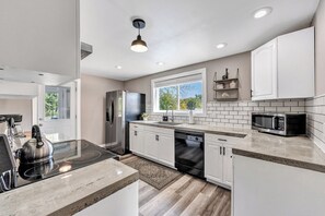 A modern kitchen with white cabinets, a stainless steel refrigerator, a microwave, and a dishwasher. - Lazy River Villa - Hottub! Fenced Yard! Sleeps 13! (Oconto)