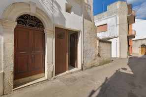 Una calle estrecha con un edificio que presenta una puerta de madera grande y otra más pequeña, ambas con manijas de metal.