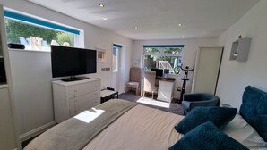 Ett modernt sovrum med en stor säng, en tv på en byrå, ett skrivbord med en stol och en motionscykel.