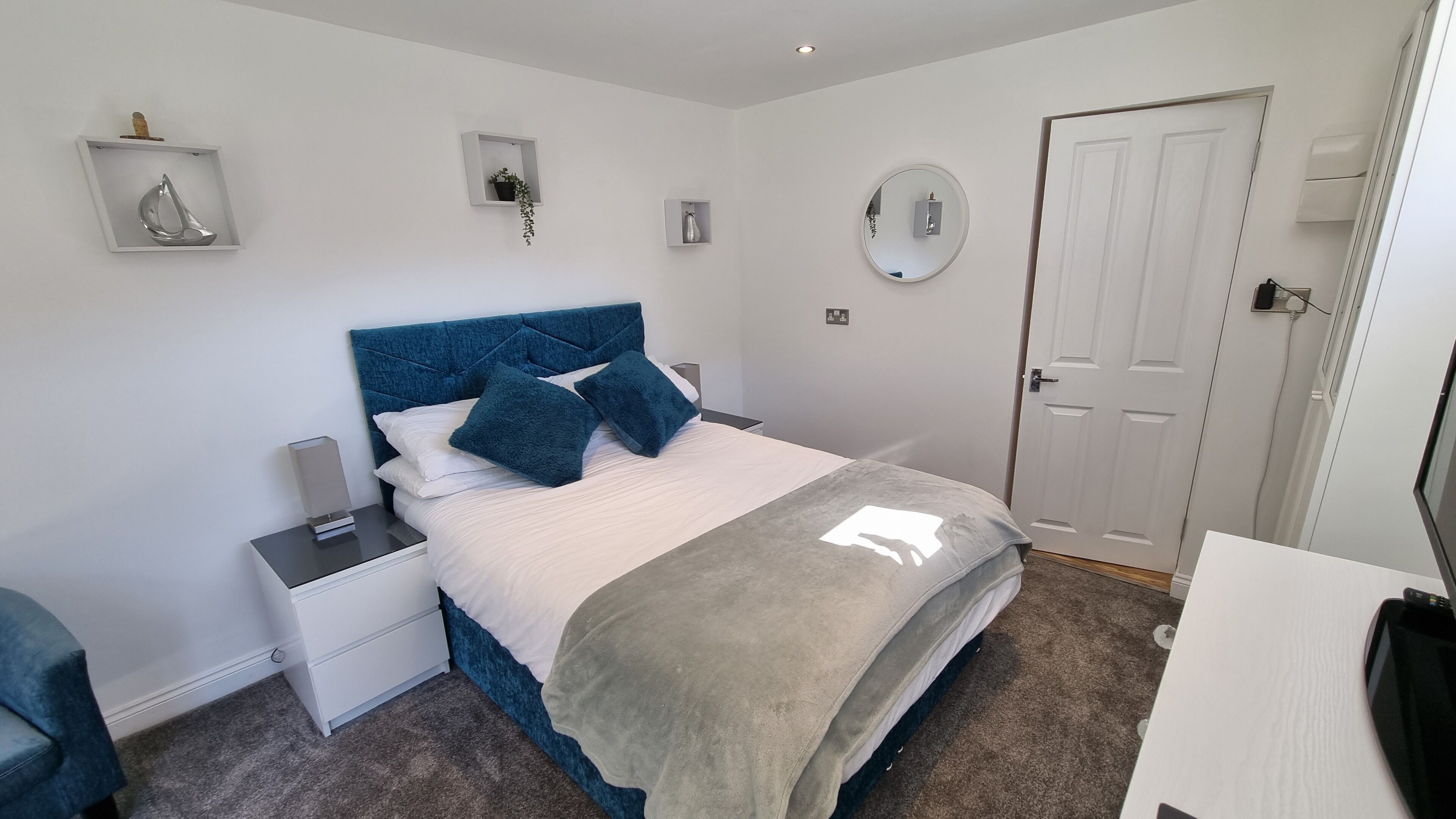 Une chambre à coucher comprenant un lit, des tables de chevet, une commode, un bureau, une chaise, une porte et un miroir fixé au mur.