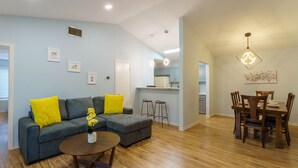 A modern living room with a gray sectional sofa, yellow pillows, a round coffee table, and a dining area with a wooden table and chairs. - King Suite, Family Friendly & Outdoor Pool Table (Austin)