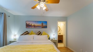 A hotel room with a bed, a ceiling fan, a cityscape painting, and a nightstand with a lamp. - King Suite, Family Friendly & Outdoor Pool Table (Austin)