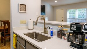 A modern kitchen with a stainless steel sink, a coffee maker, and a wall-mounted TV. - King Suite, Family Friendly & Outdoor Pool Table (Austin)