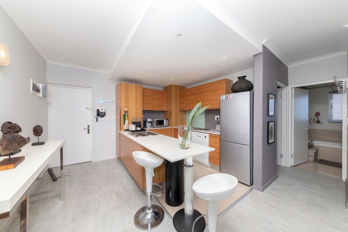 Una cucina moderna con isola centrale, sgabelli da bar ed elettrodomestici contemporanei.