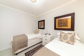 A bedroom with two beds, a bedside table, a lamp, and a patterned wall hanging. - West Coast Horizon Retreat (Cape Town)