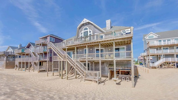 Une propriété située en bord de mer, comprenant plusieurs niveaux, des balustrades en bois et un escalier imposant menant aux étages supérieurs.