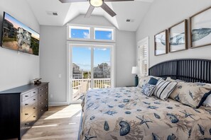 A bedroom with a large bed, a ceiling fan, a dresser, and a view of houses through a sliding door. - Semi-Oceanfront Dog Friendly w/ Pool, Hot Tub, Tiki Bar, Game Room, Beach Nearby (Avon)