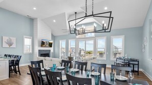Un comedor espacioso con techo alto, ventanas amplias que dan a la playa y una lámpara moderna.