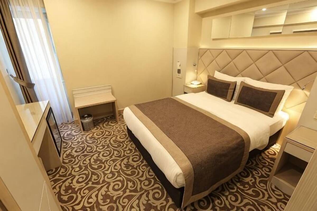A hotel room with a bed, bedside table, lamp, and a patterned carpet.
