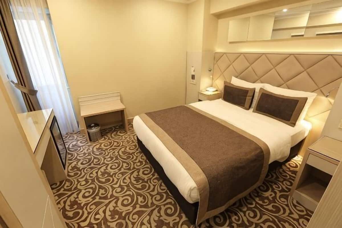 A hotel room with a bed, bedside table, lamp, and a patterned carpet.