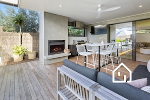 An outdoor patio with a built-in fireplace, white chairs, and a wooden deck.