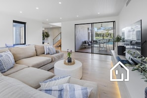 A modern living room with a sofa, coffee table, and a dining area with outdoor seating.