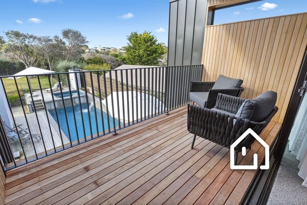 A wooden deck with a pool, a chair, and a view of the surrounding area.