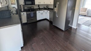 A modern kitchen with white cabinets, stainless steel appliances, and dark wooden flooring. - Spacious 3 Bedroom, 5 minutes from Downtown Cincinnati (Highland Heights)