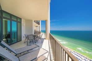 A balcony with a view of the ocean, a seating area with chairs and tables, and a glass door leading to an interior space.