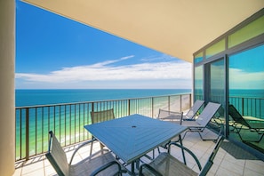 A balcony with a table and chairs, overlooking the ocean.