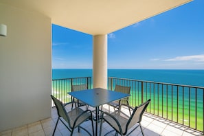 Varanda com mesa e cadeiras, com vista para um mar azul e límpido.