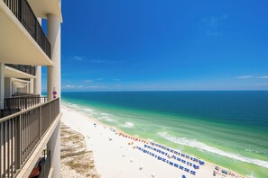 A beach view from a balcony with a clear sky, ocean, and beach umbrellas.