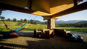 A rustic outdoor seating area with a stone pillar, wooden furniture, and a hammock under a wooden roof. - Quadruple Room with Bathroom (Sciegny)
