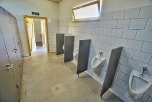 A public restroom with multiple urinals, a tiled floor, and a door leading to another room. - Quadruple Room with Bathroom (Sciegny)