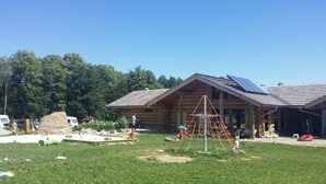 A log cabin with a sloped roof and solar panels, surrounded by a grassy yard with a playground. - Quadruple Room with Bathroom (Sciegny)