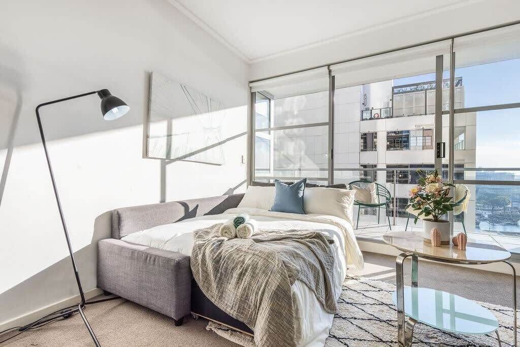 A modern bedroom with a bed, bedside table, and a large window offering a city view.