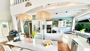 Une cuisine moderne avec des meubles blancs, un îlot central doté de sièges et une vue sur la verdure à l’extérieur.