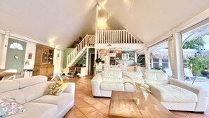 Un vaste espace de vie agrémenté de canapés blancs, d’une table basse en bois et d’un escalier menant à un niveau supérieur.