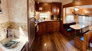 A compact RV kitchen with wooden cabinets, a sink, and a dining area with a bench.