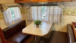 A cozy RV interior with a central table, two seating areas, and a potted plant.