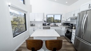 A modern kitchen with white cabinets, a stainless steel refrigerator, and a large window overlooking a scenic view.