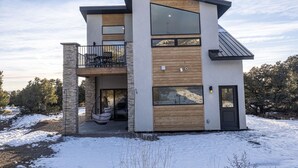 A modern two-story house with a balcony, large windows, and a stone pillar.