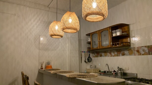 Una cucina con isola centrale, lampade a sospensione in vimini, pensili in legno e un piano cottura.