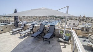 Terraza en la azotea con sillones de descanso y un gran paraguas, con vistas a un puerto deportivo y al paisaje urbano.