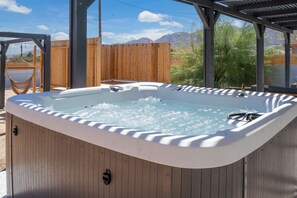 A hot tub under a wooden pergola with a wooden fence and mountains in the background.